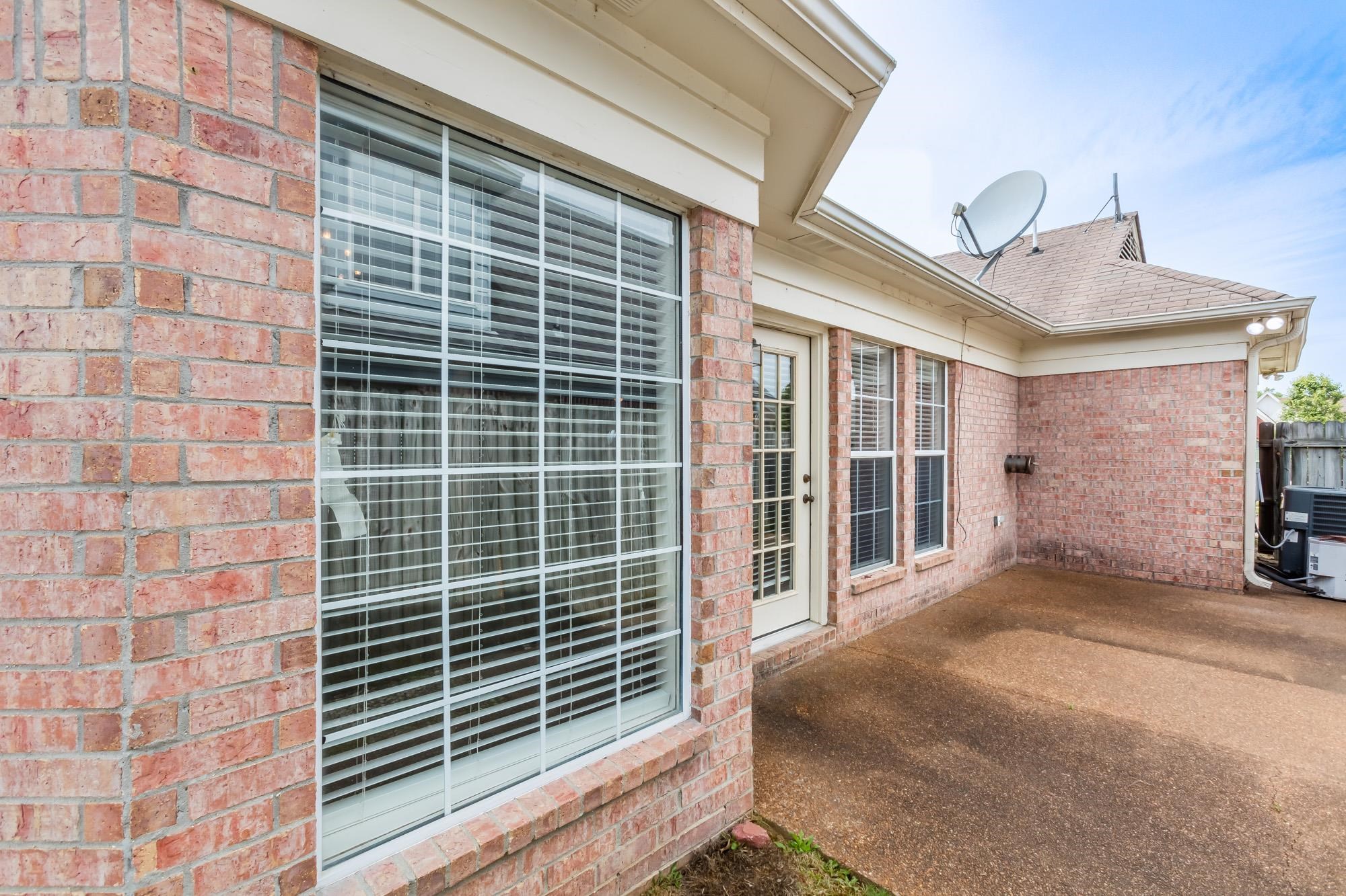 Brick home’s covered patio with large windows, a glass door, and a satellite dish on the roof.