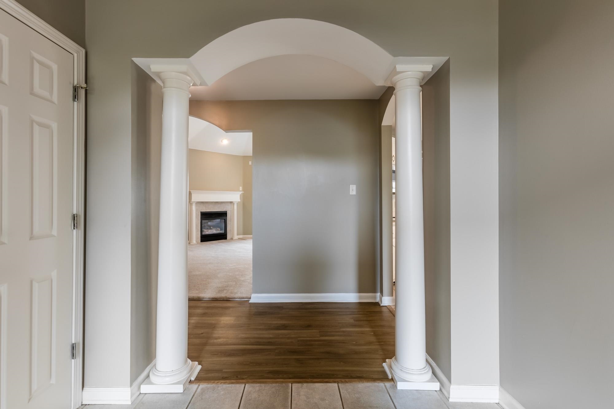 Entry hall with a white columned arch, dark wood floors, and a view of a fireplace.