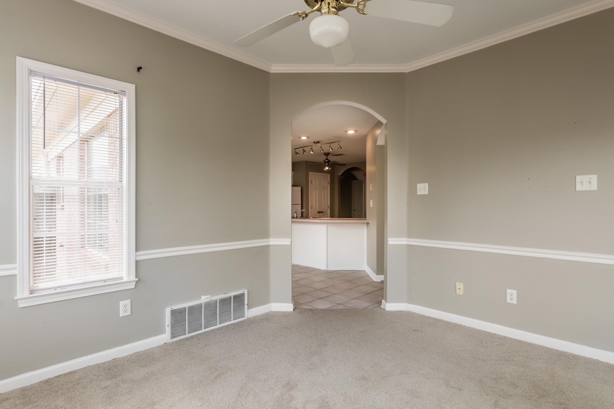 Empty carpeted living room with a window and an arched opening to the kitchen.
