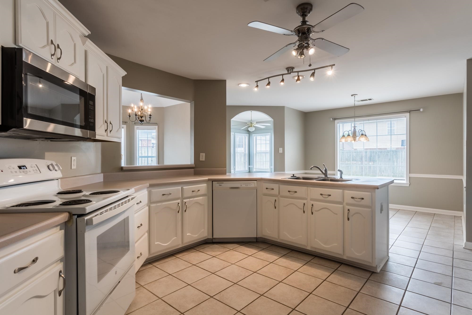 Kitchen with white cabinets, tiled floor, corner sink beneath a large window, and an arched opening.