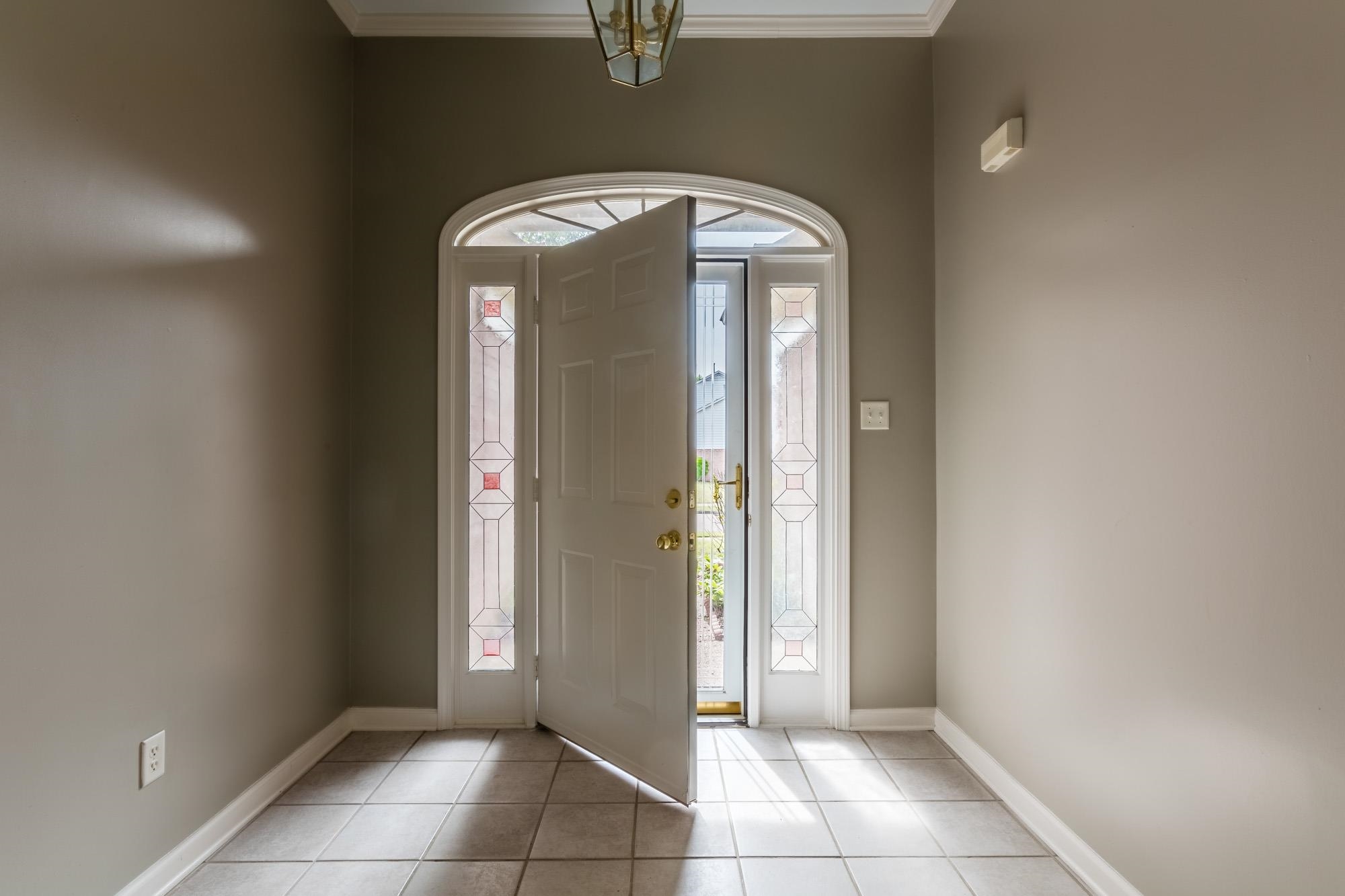 Entry foyer with tiled floor and open front door framed by decorative sidelights and an arched transom.