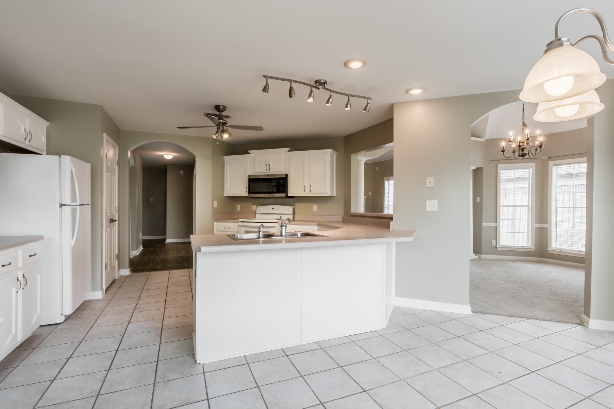 Kitchen with white cabinets, a large sink peninsula, tile flooring, and an adjoining dining area.