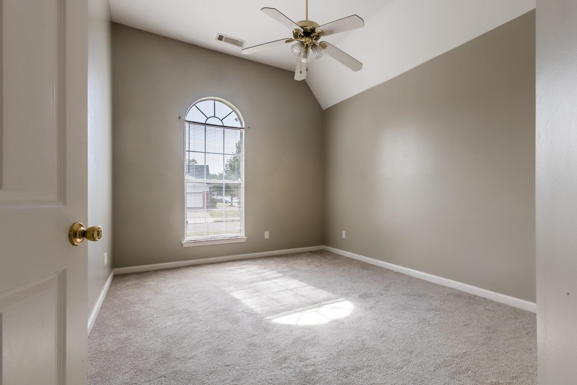 Vacant bedroom with a vaulted ceiling, ceiling fan, and tall arched window.