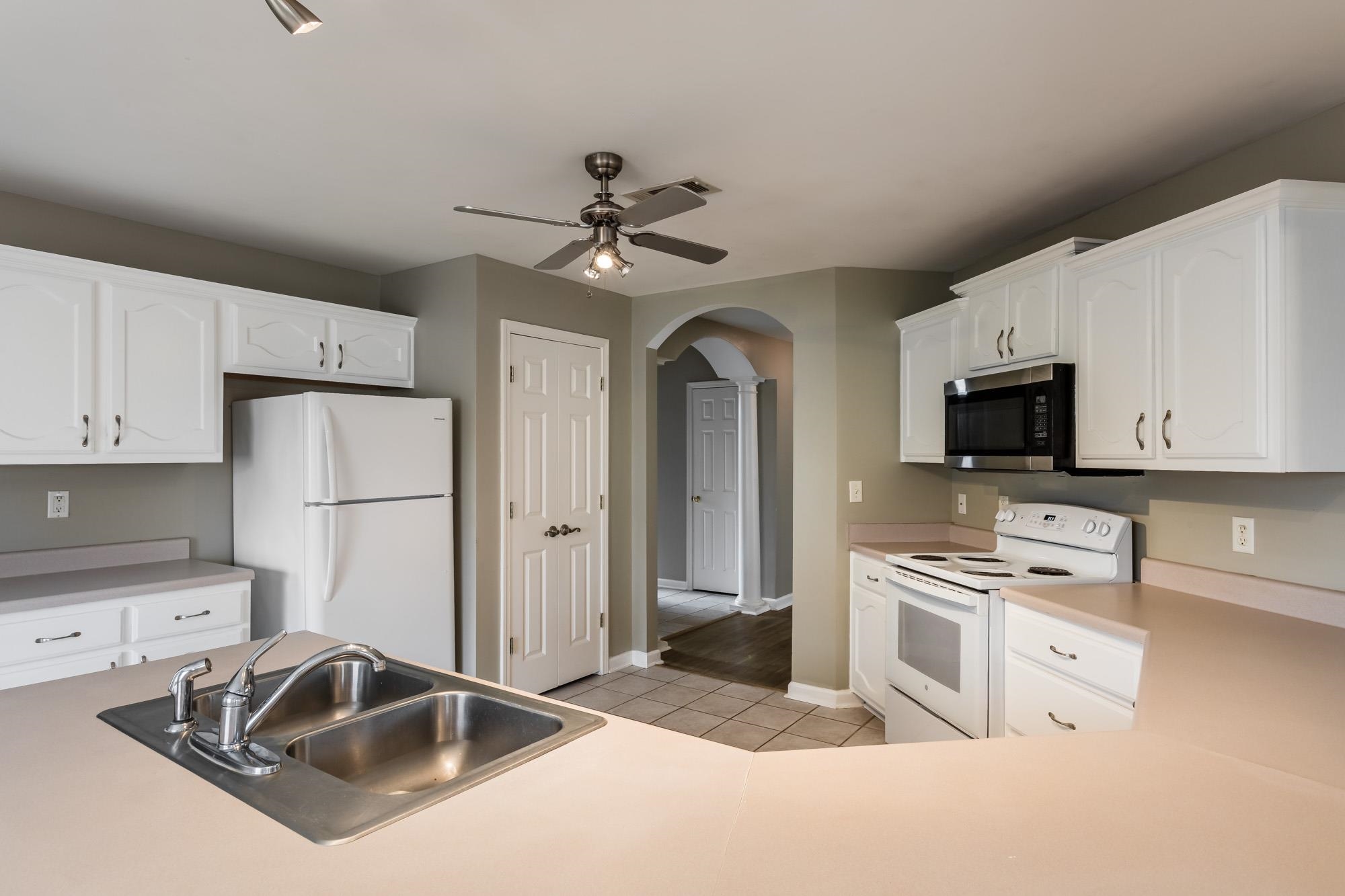 Kitchen with white cabinets, double-basin sink, and an arched doorway to the hall.