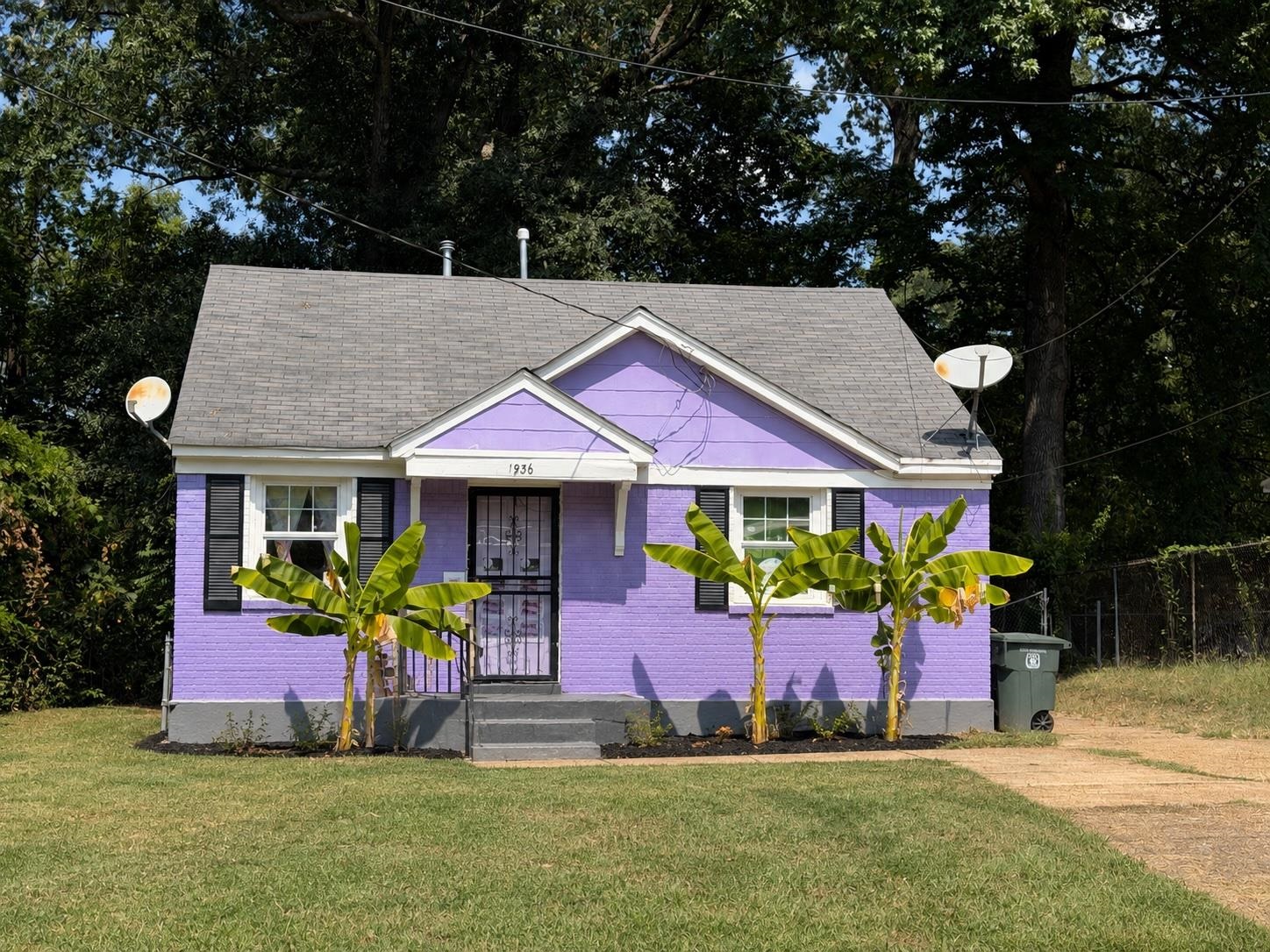 Purple brick house with a gray gable roof and banana plants along the front facade.
