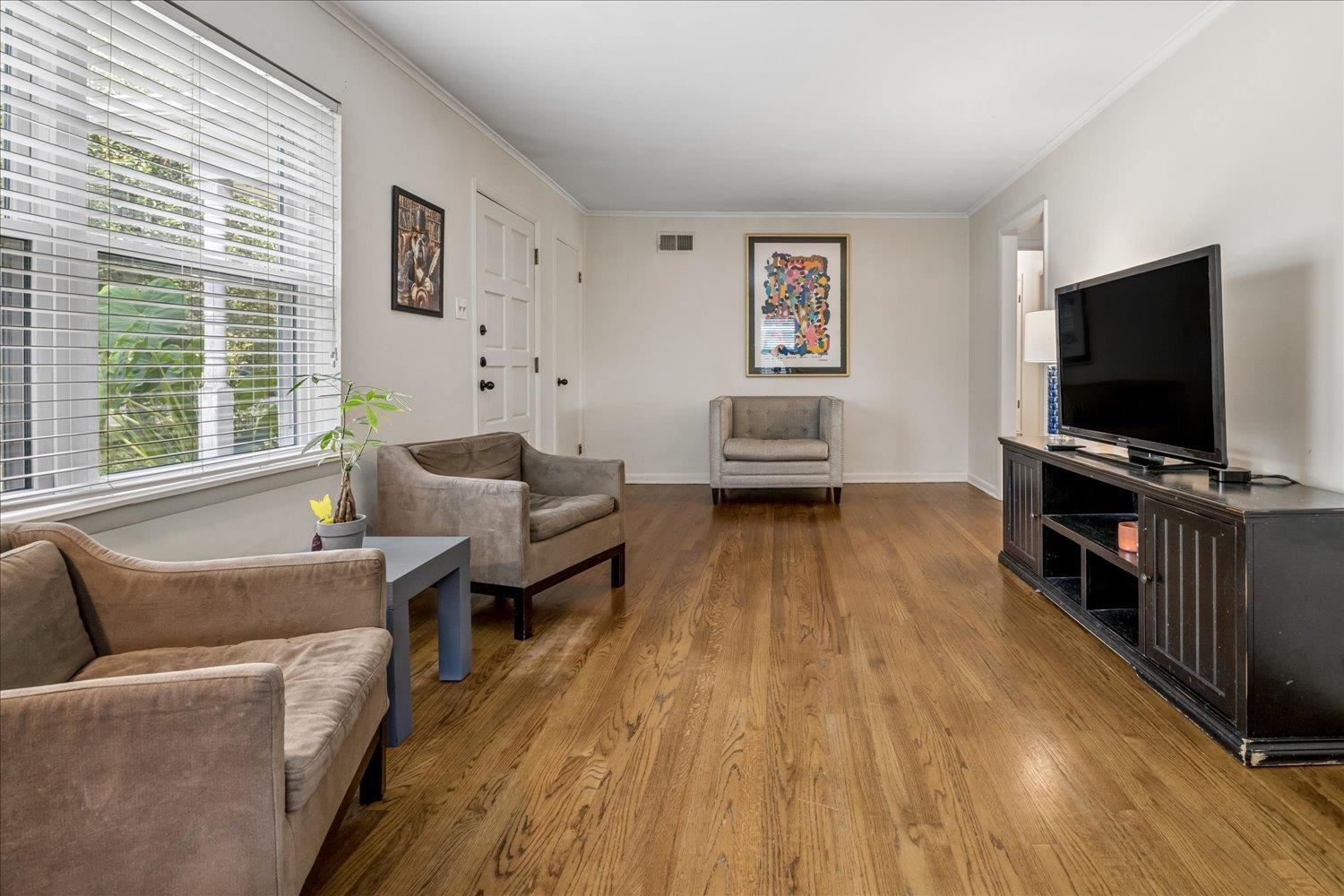 Living room with hardwood floors, taupe armchairs, a large window, and a television.