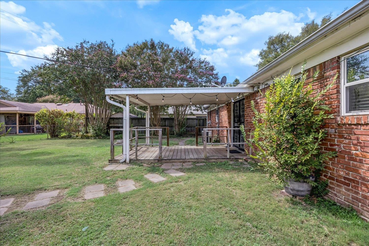 Brick home backyard with a covered wooden deck, string lights, and a grassy lawn.