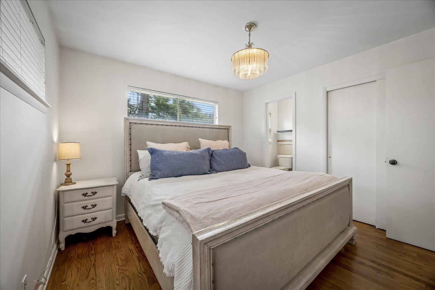 Furnished bedroom with a large upholstered bed, hardwood floors, and a chandelier.