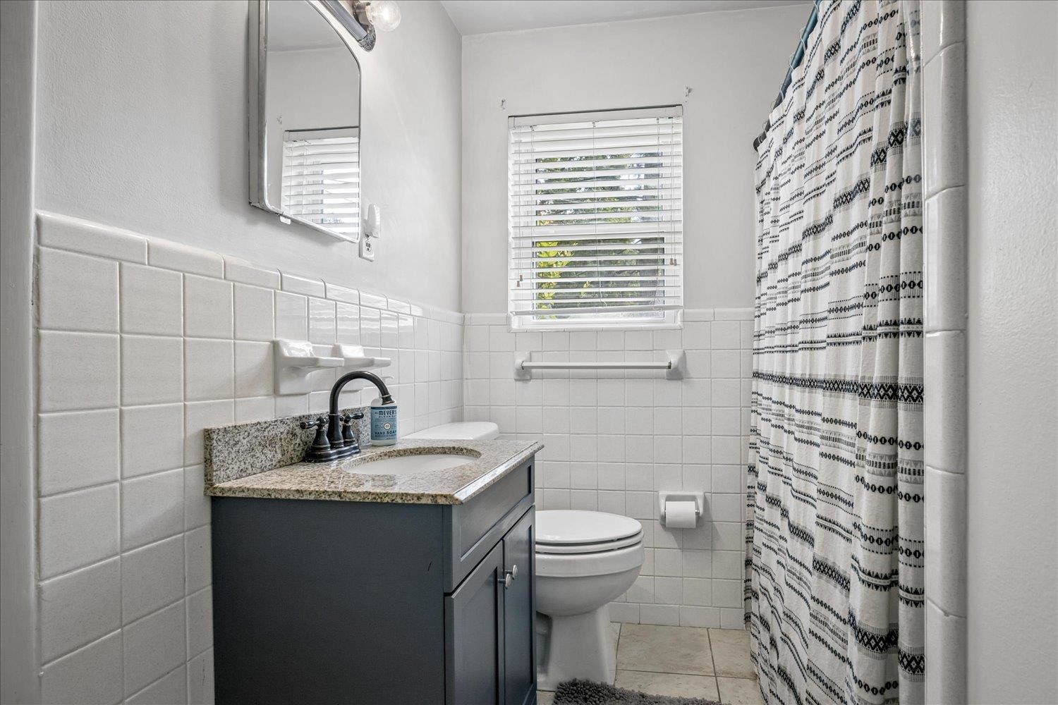 Bathroom with a dark blue vanity, white tile, and a black-and-white patterned shower curtain.
