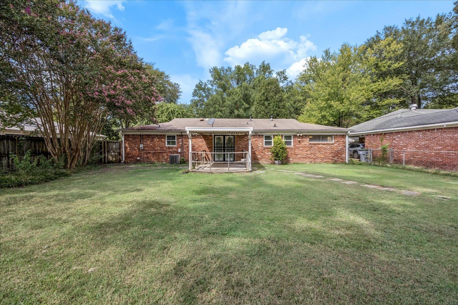 Brick home’s rear exterior with a covered wooden porch and broad grassy backyard.