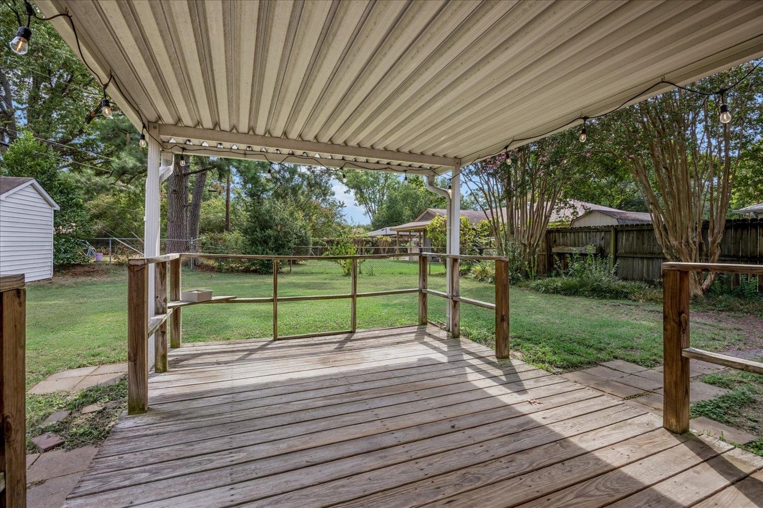 Covered wooden deck with string lights overlooking a grassy, fenced backyard.