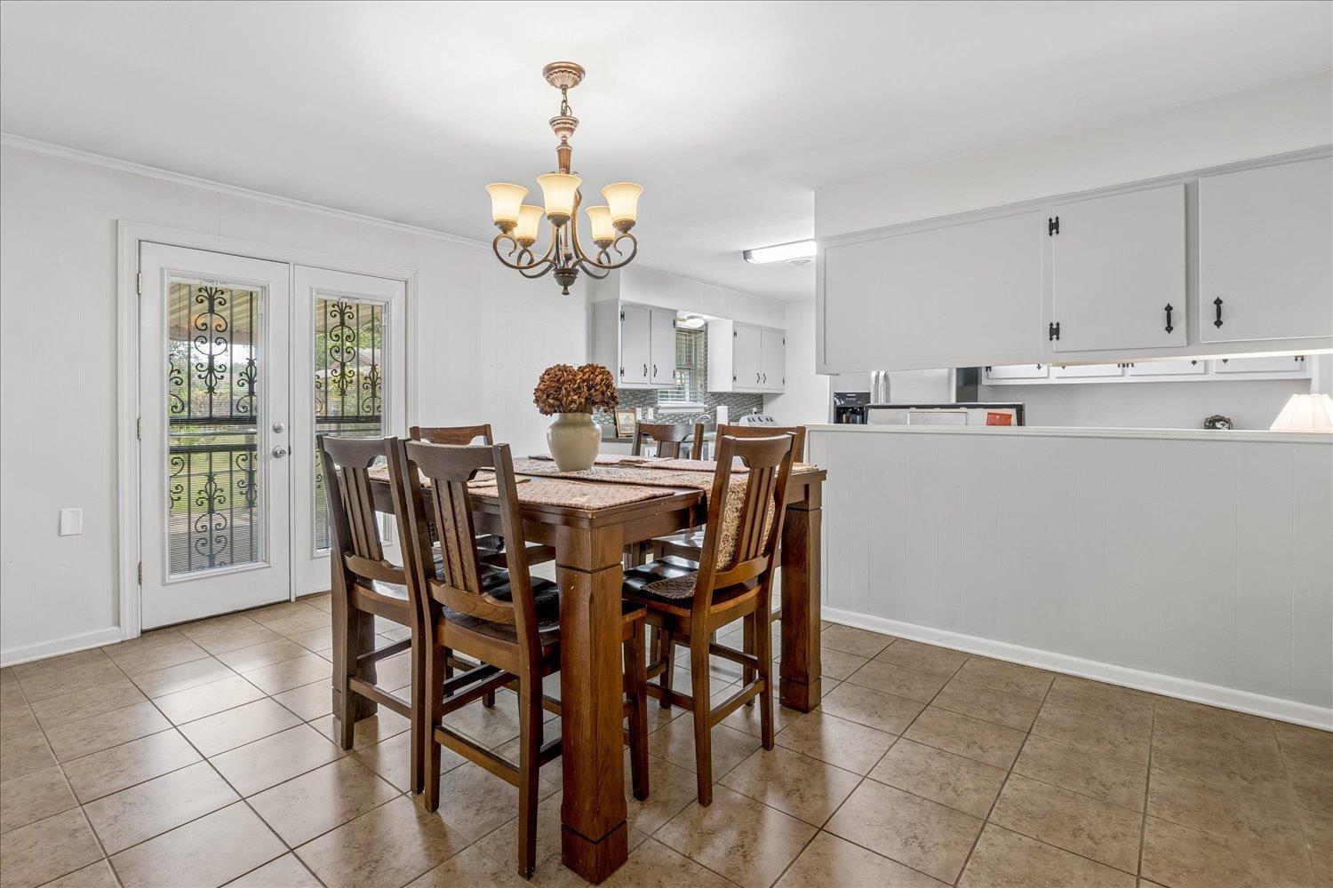 Dining area with a dark wood table beneath a chandelier, opening into a white-cabinet kitchen.