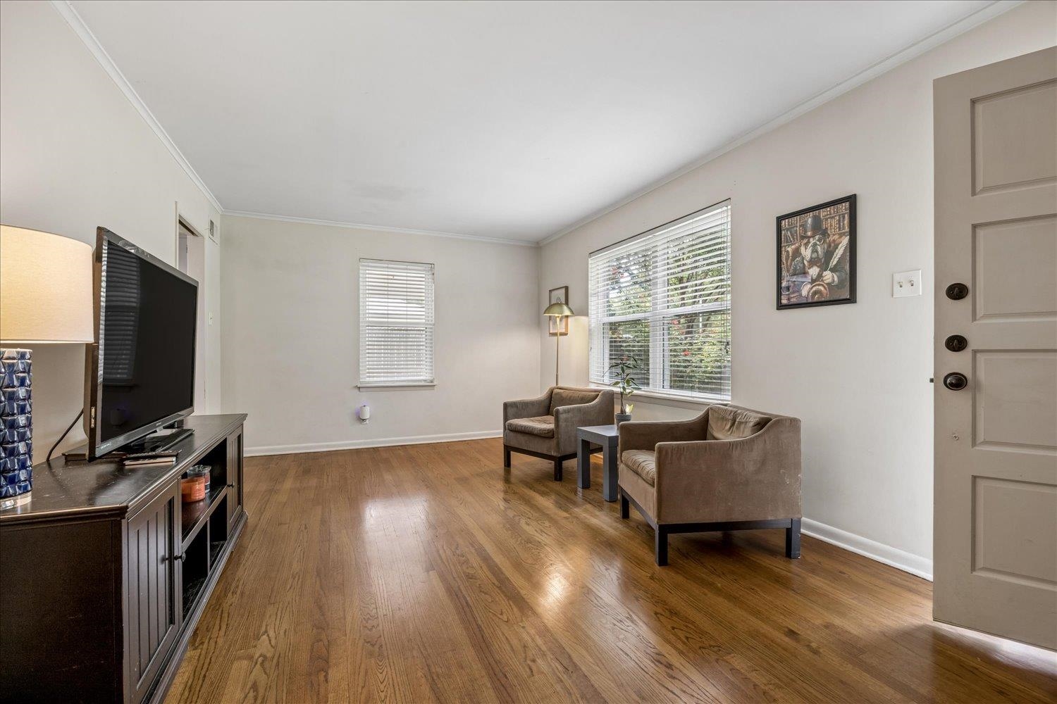 Living room with hardwood floors, two armchairs, and a large window with blinds.