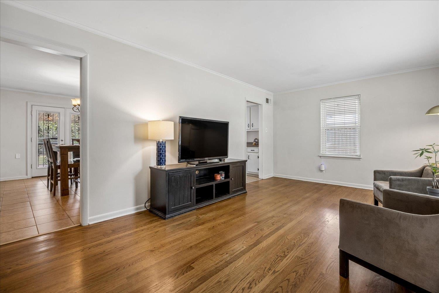 Living room with hardwood floors, TV console, and a view into the tiled dining area.