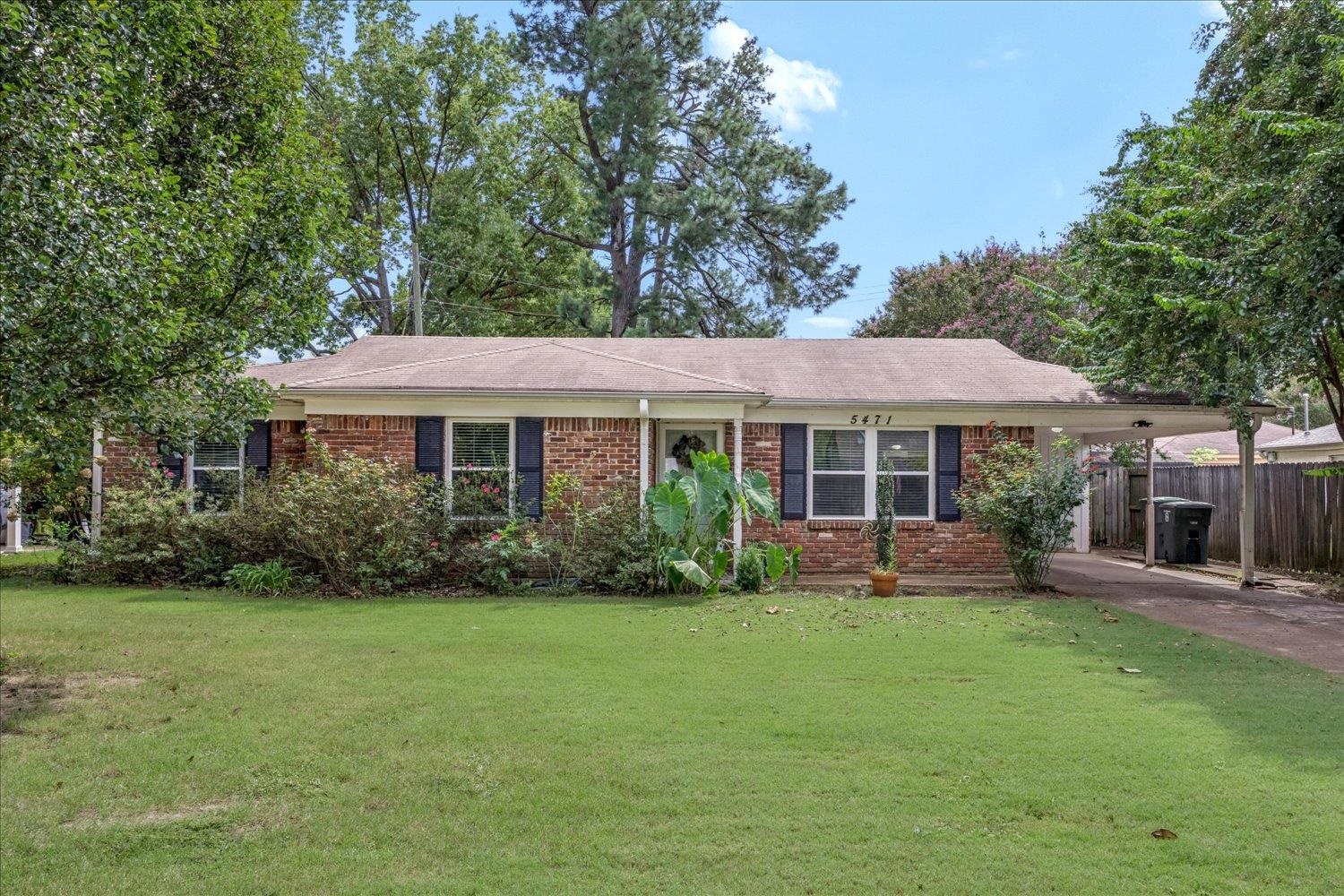 Single-story brick home with a broad front lawn, mature trees, and an attached carport.