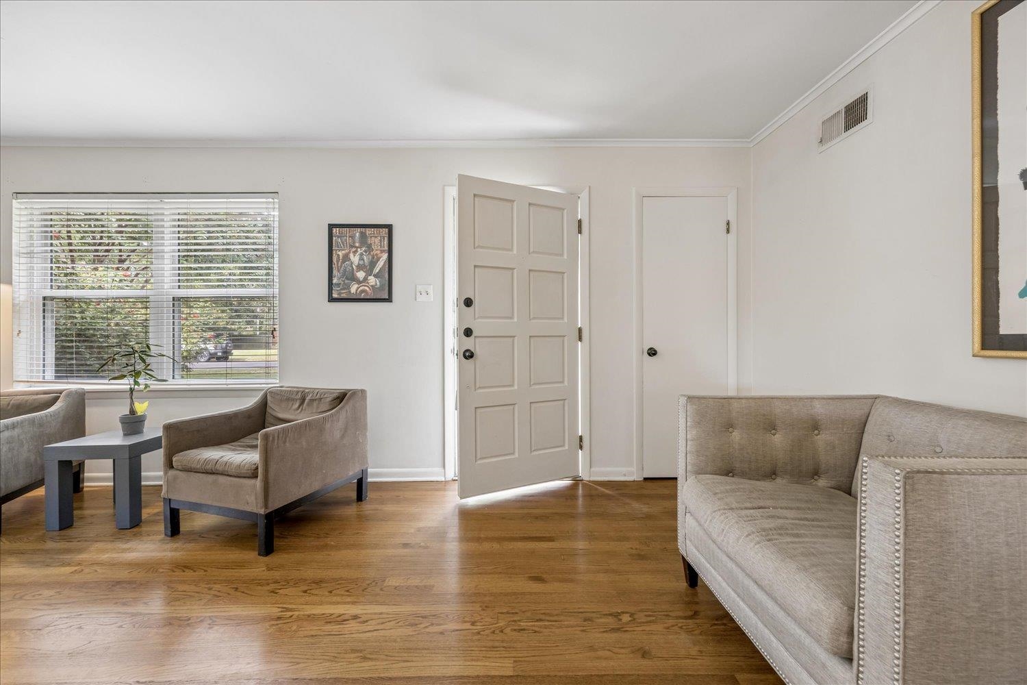 Living room with hardwood floors, neutral seating, and an open front door.
