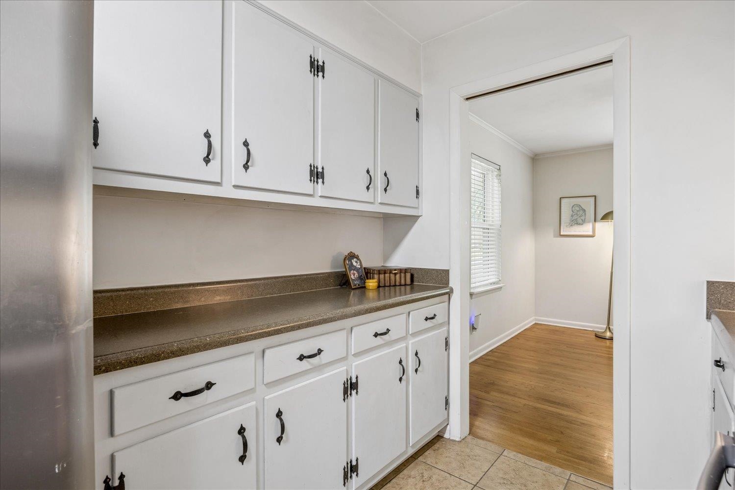 Kitchen with white cabinets and dark countertops, opening into a room with hardwood floors.
