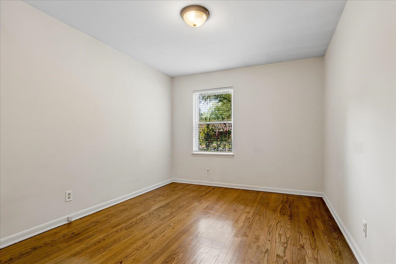 Empty room with polished hardwood floors and a window with blinds.