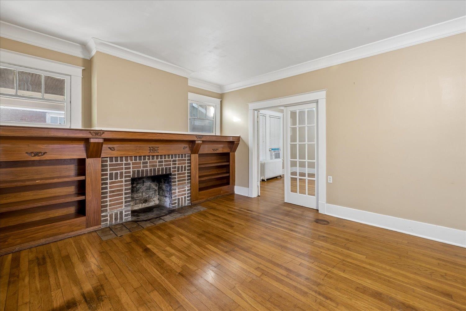 Living room with a brick fireplace, built-in wooden shelves, and polished hardwood floors.