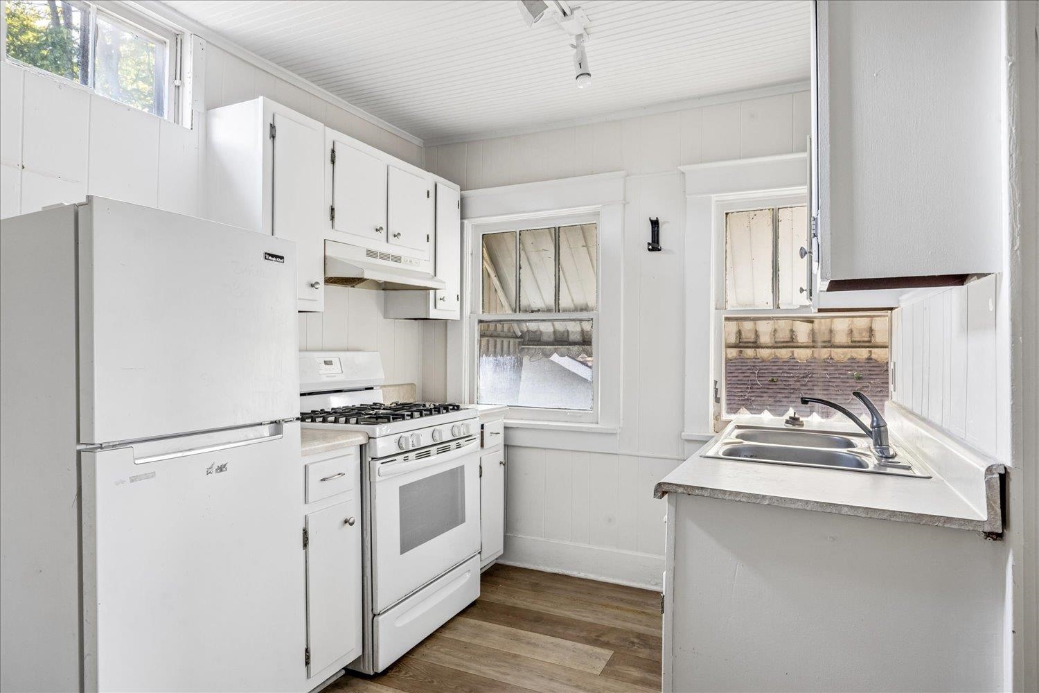White kitchen with a gas range, refrigerator, and double-basin sink beneath windows.