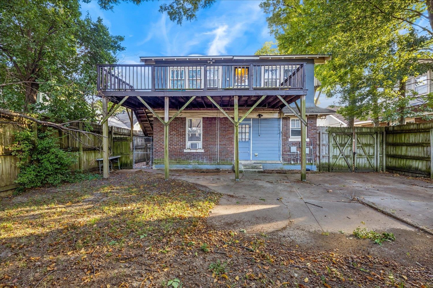 Brick house with an elevated wooden deck overlooking a fenced backyard and concrete patio.