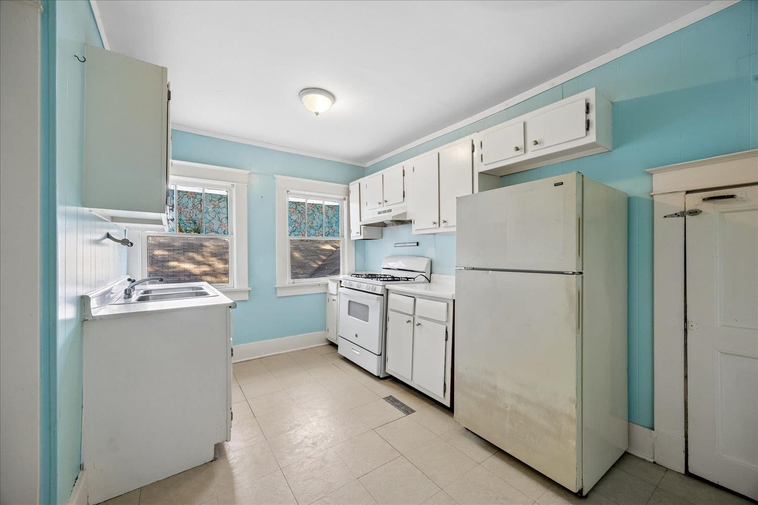 Kitchen with turquoise walls, white cabinets, a gas range, and two windows with decorative glass panels.