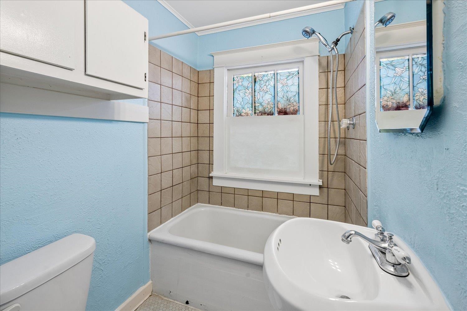 Bathroom with a bathtub, beige tiled shower surround, and floral stained-glass window.