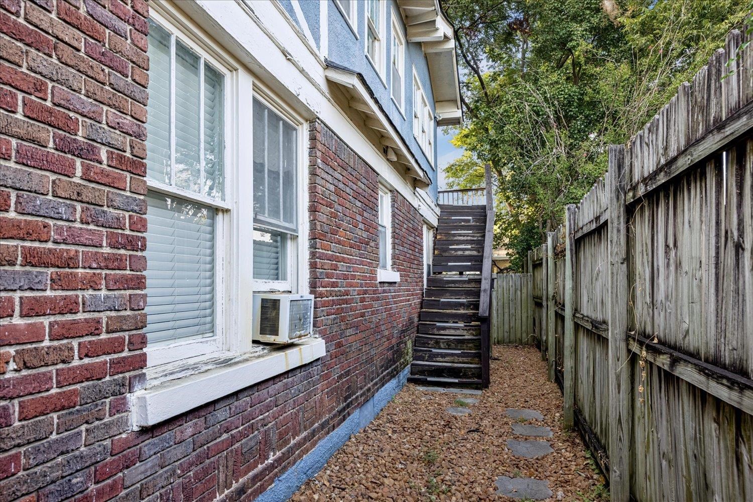 House side passage with brick walls, wooden stairs, and a tall fence.