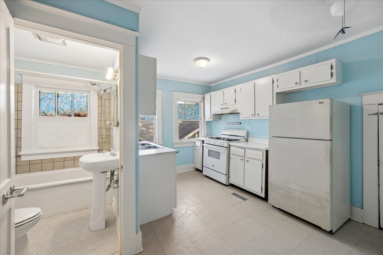 Kitchen with white cabinets and appliances beside a bathroom with a pedestal sink and bathtub.