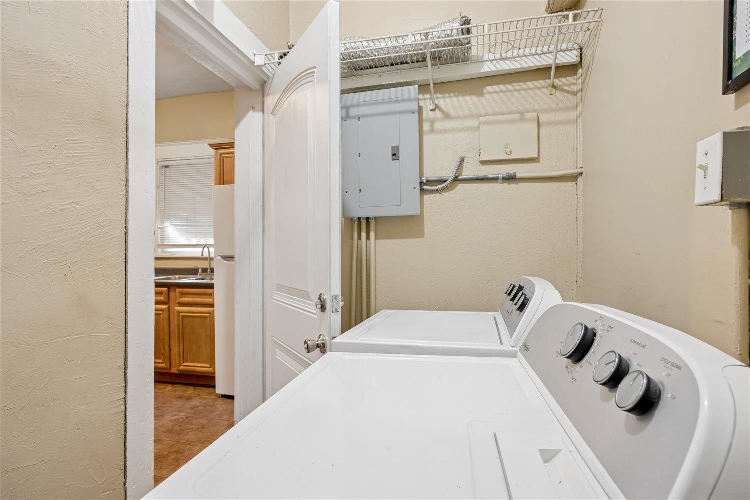Laundry room with a white washer and dryer, overhead wire shelf, and electrical panel.