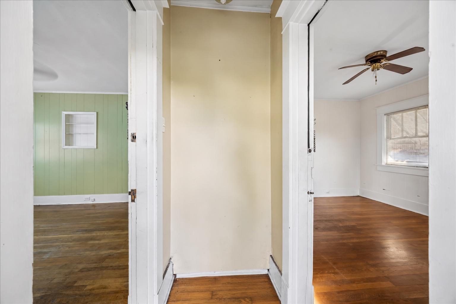 Hallway opening onto two unfurnished rooms, with hardwood floors and pale green paneling in one room.