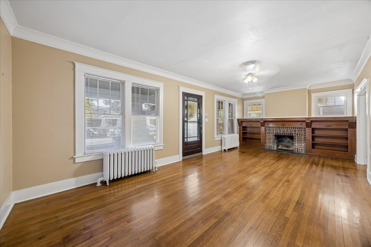 Empty living room with hardwood floors and a brick fireplace between built-in bookshelves.