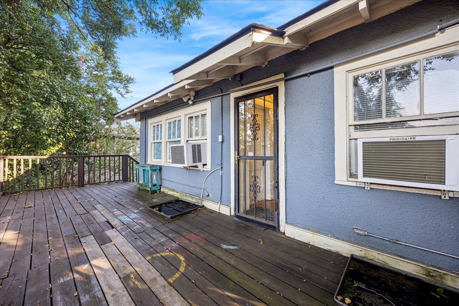Blue house exterior with a weathered wooden deck, screened door, and window air conditioners.