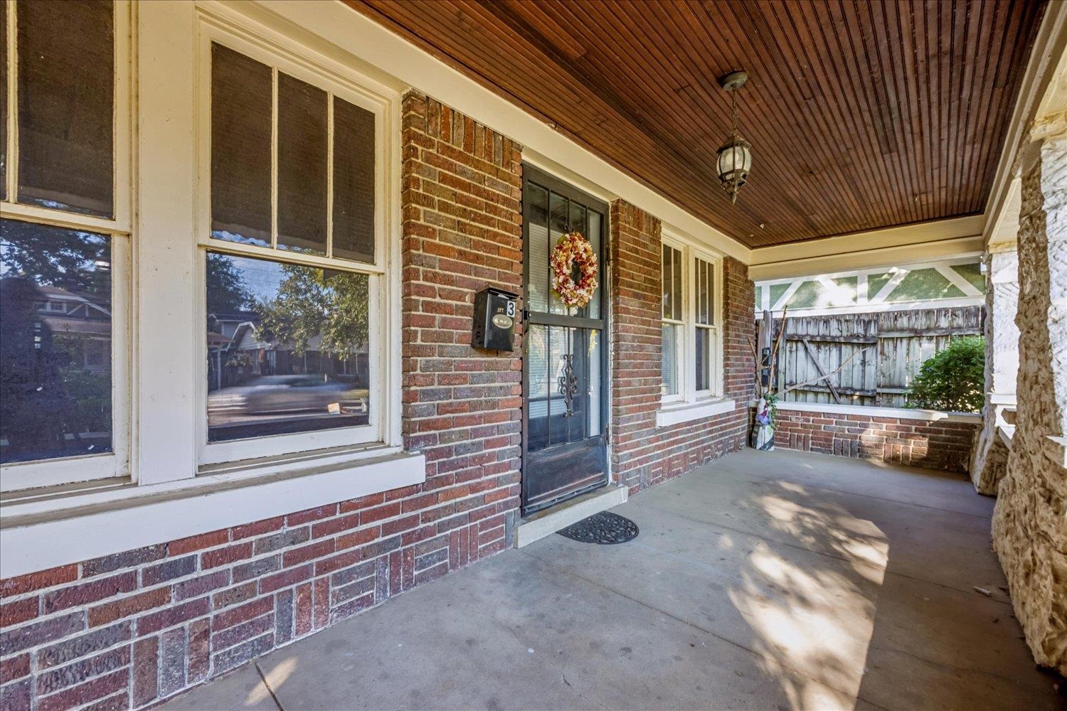 Brick front porch with a wreath on the entry door and a wood-plank ceiling.
