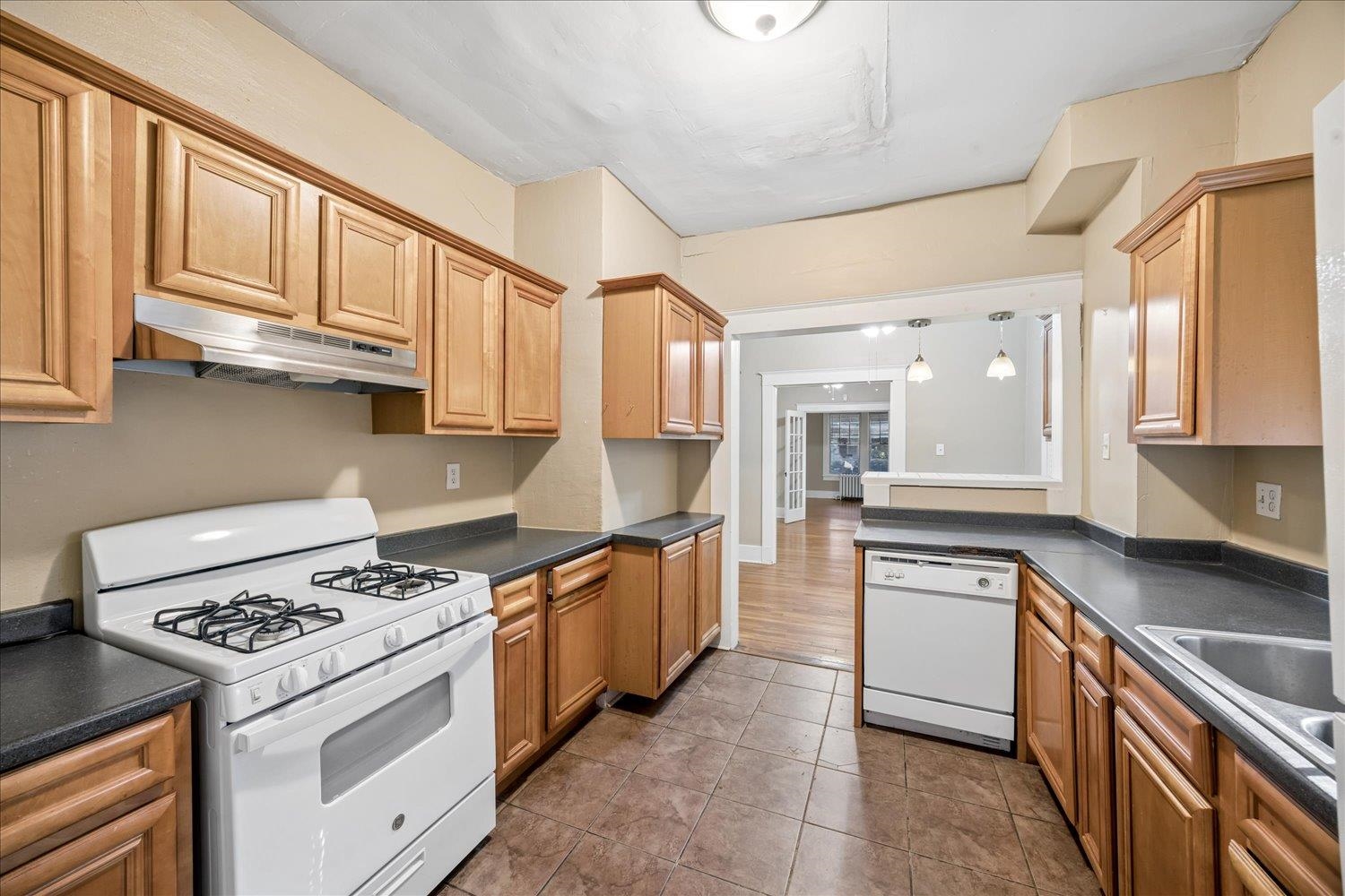 Kitchen with light wood cabinets, dark countertops, a white gas range, and a wide pass-through.