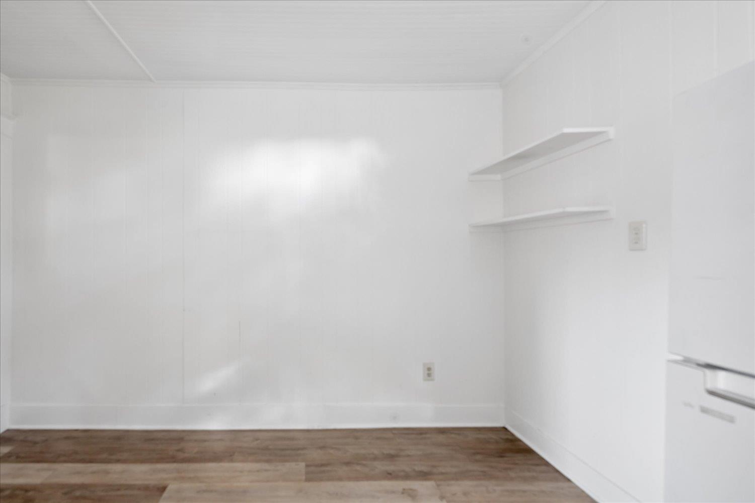 Empty kitchen with floating shelves, white cabinetry, and brown wood-look flooring.