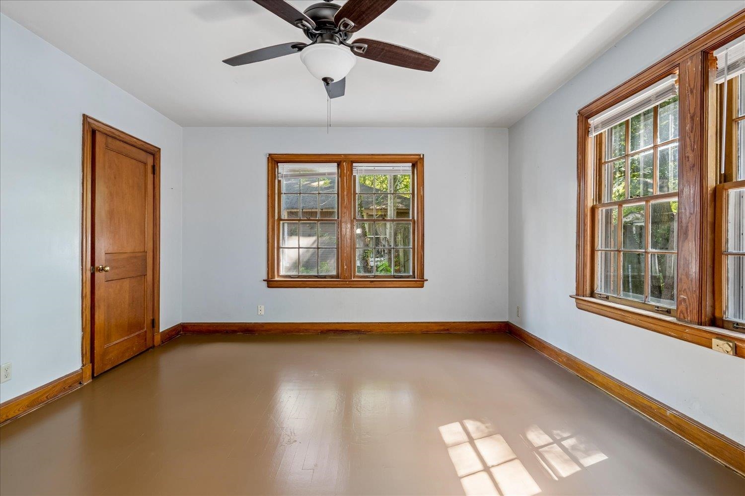 Empty room with wood-trimmed windows, pale blue walls, and a ceiling fan.