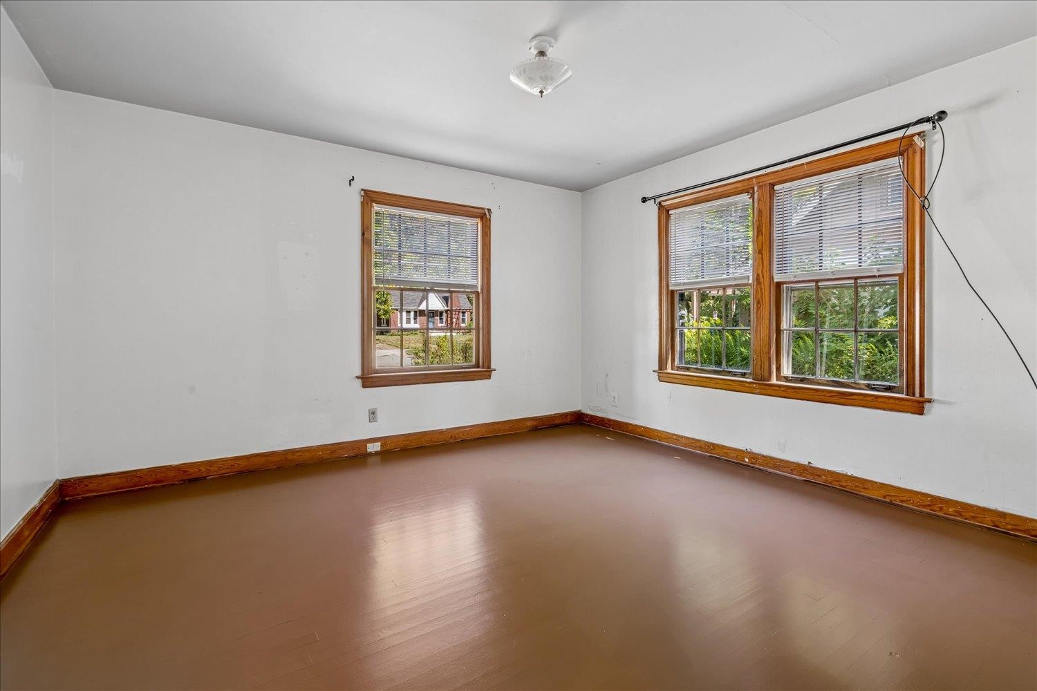 Empty room with brown flooring and three wood-trimmed windows with blinds.