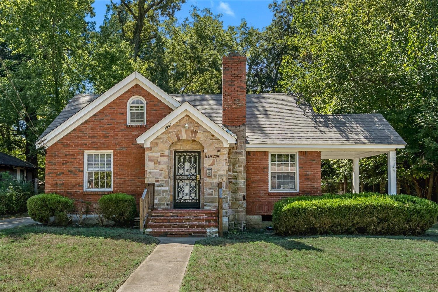 Red brick house with a stone arched entry, decorative metal door, and covered carport.