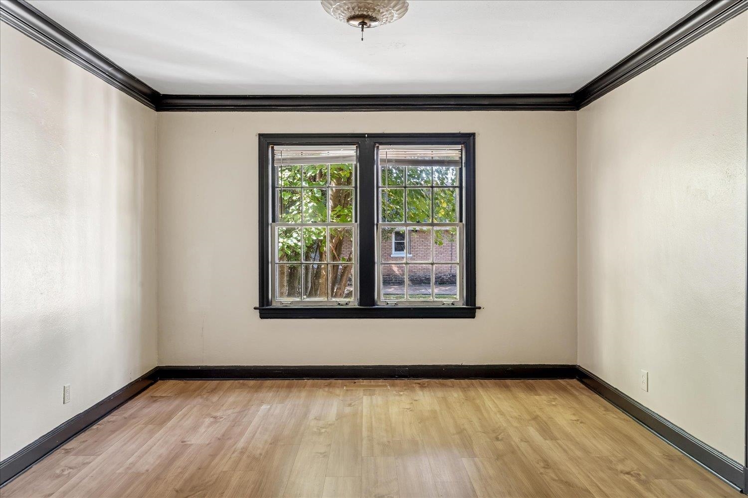 Empty room with light wood floors, black trim, and paired windows.