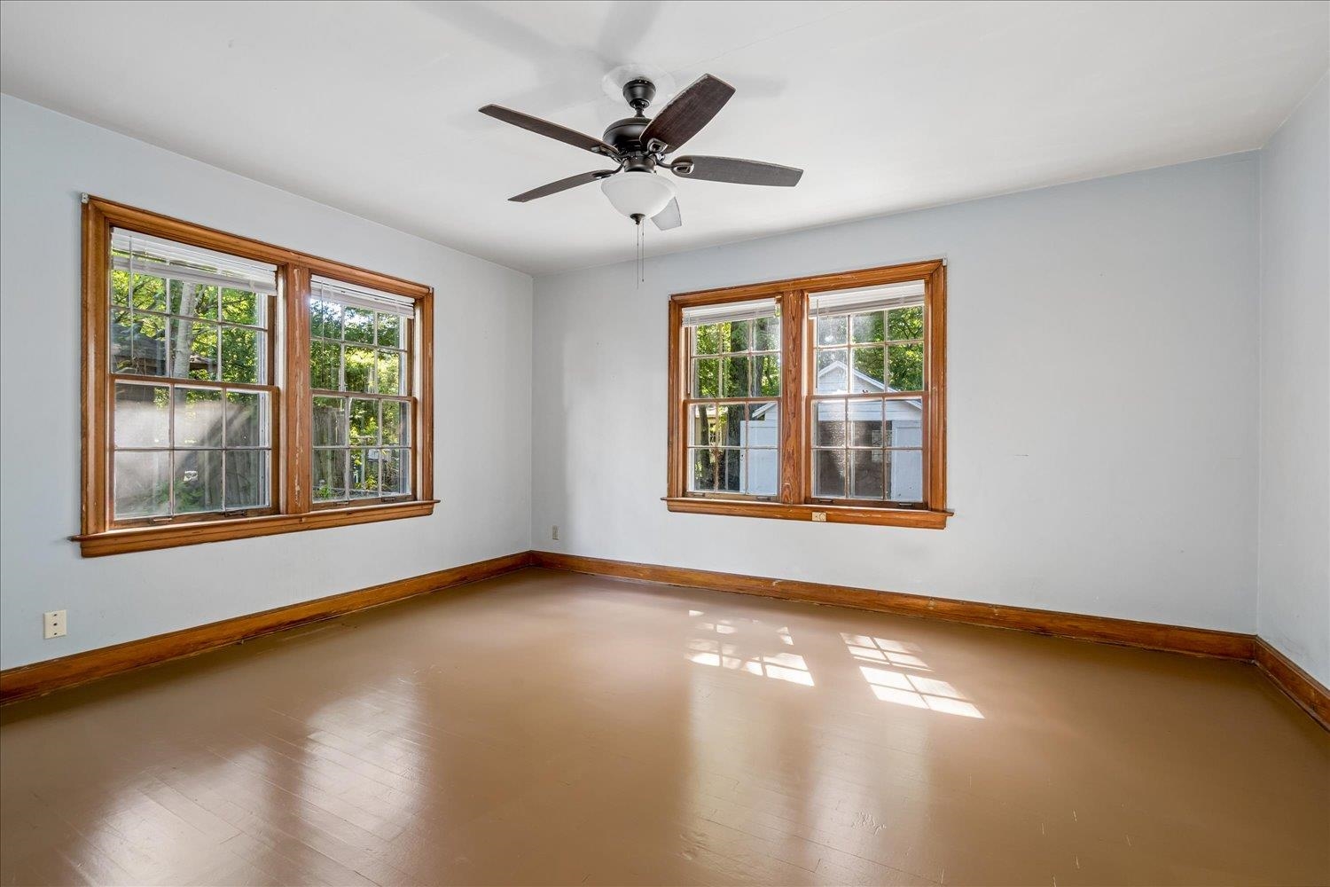 Empty room with four wood-framed windows, warm wood trim, and a ceiling fan.