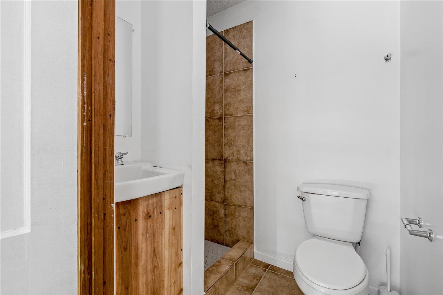 Bathroom with a wood vanity, white toilet, and brown-tiled shower.