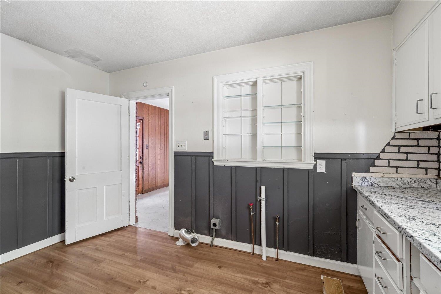 Kitchen with dark paneled walls, granite counters, exposed plumbing, and a damaged ceiling.