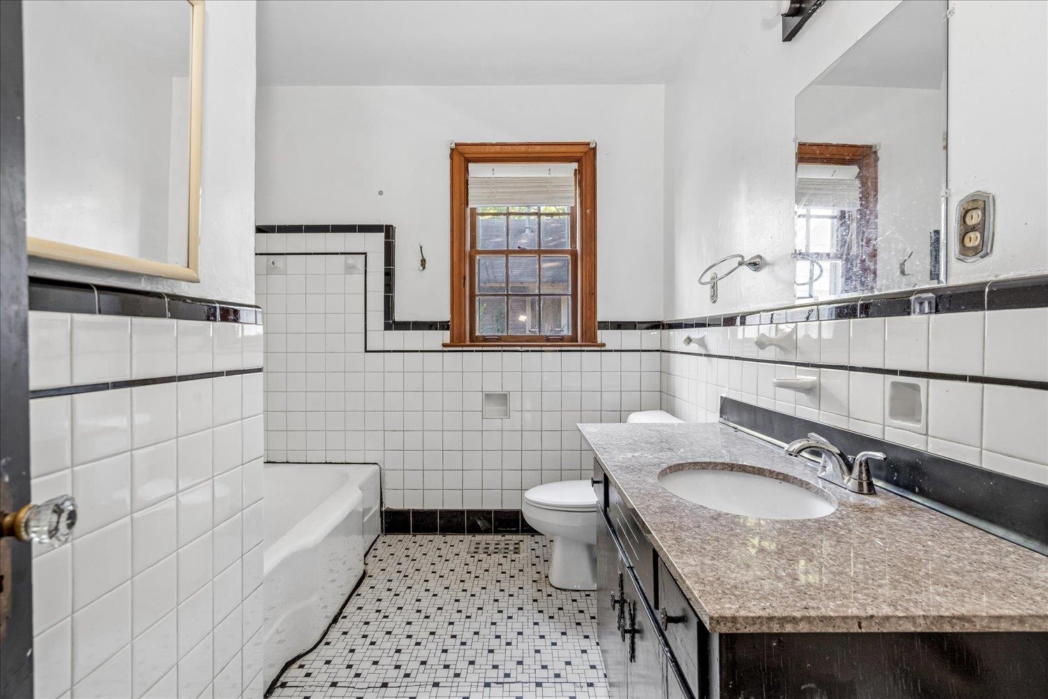 Bathroom with black-trimmed white tile, a bathtub, and a dark vanity beneath a wood-trimmed window.