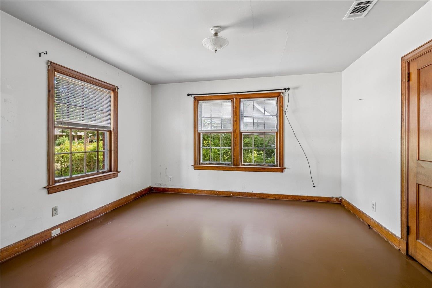 Empty room with two wood-trimmed windows, blinds, and a brown floor.
