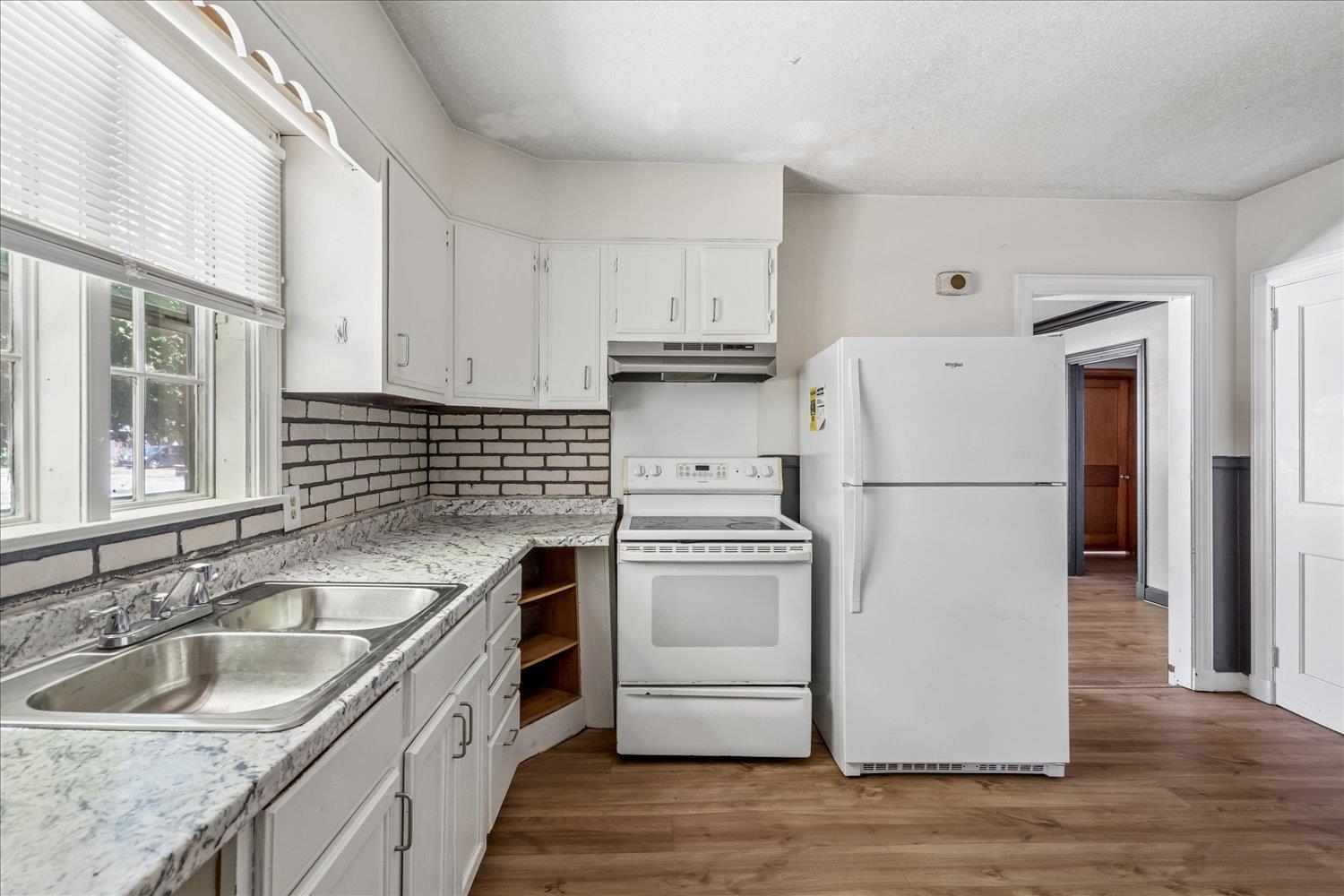 Kitchen with white cabinets, a brick backsplash, and a double-basin sink beside a large window.