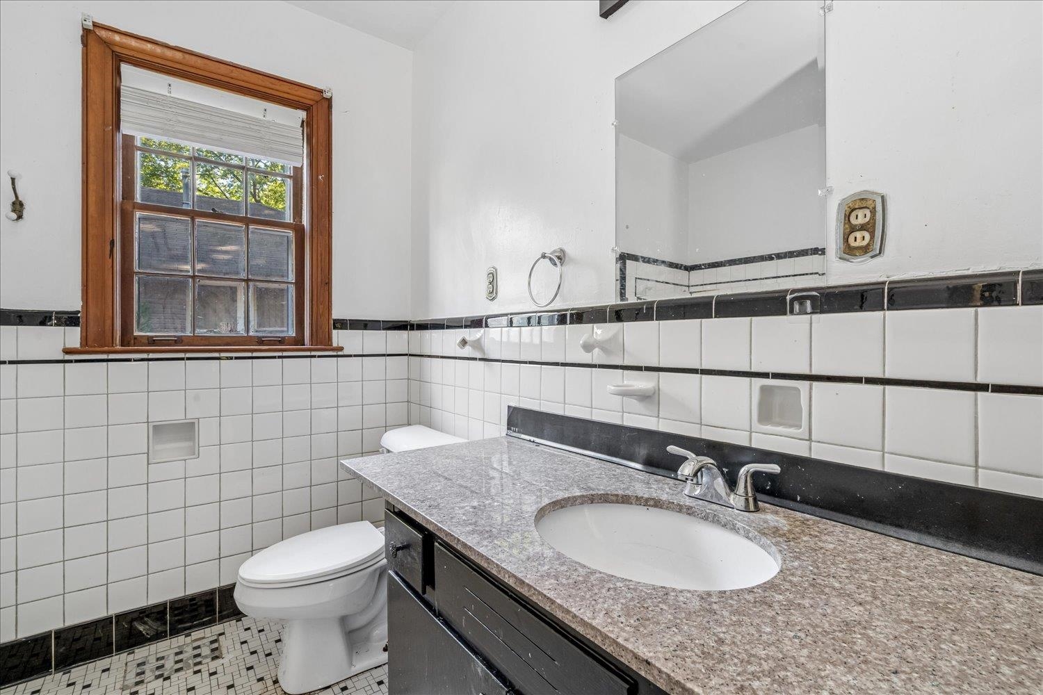 Bathroom with black-trimmed white tile, a dark vanity, and a wood-framed window.