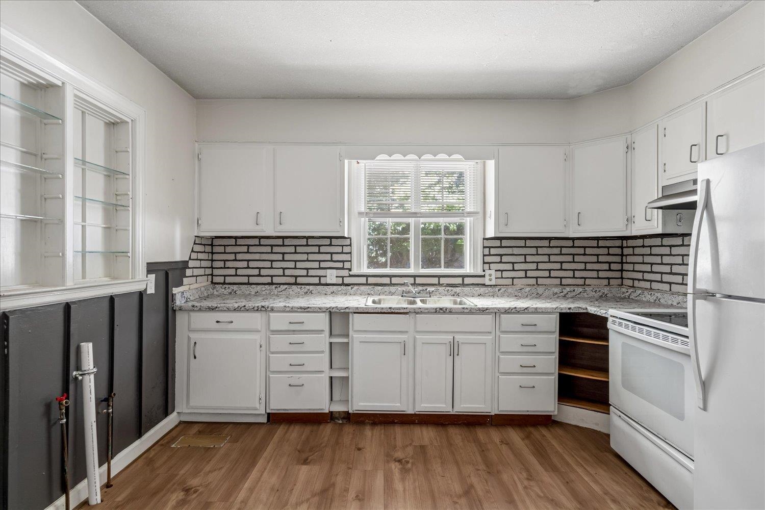 Kitchen with white cabinets, dark brick backsplash, stone countertops, and a window above the sink.