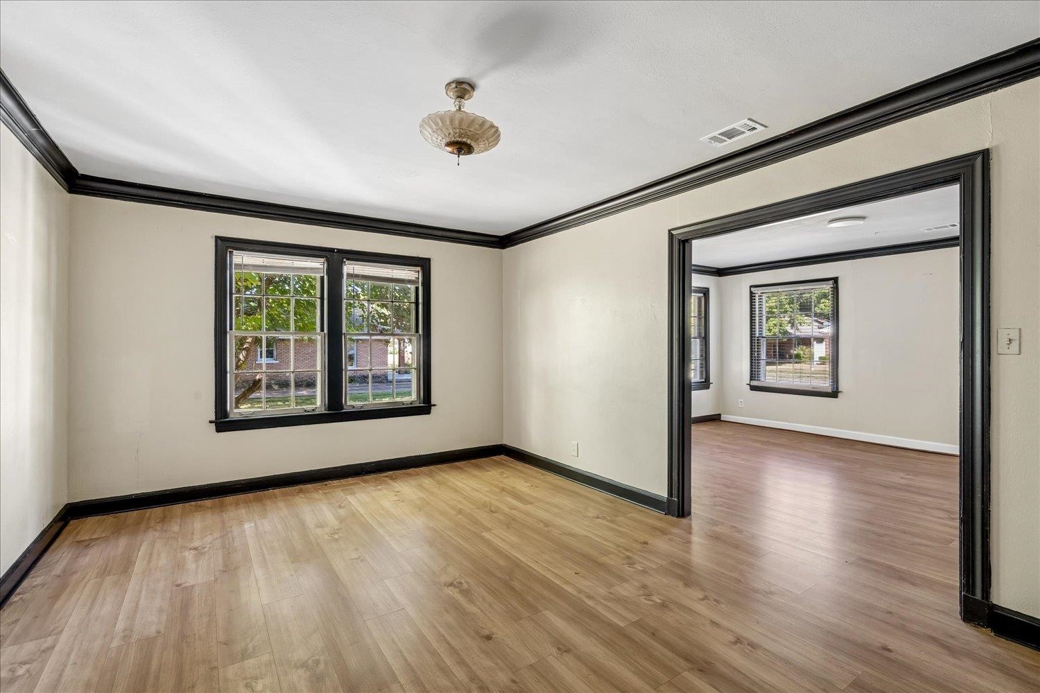 Empty room with wood floors, dark trim, and a wide doorway to a second room.