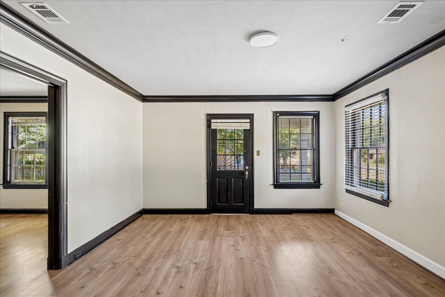 Empty room with wood-look floors, dark trim, and a black entry door between windows.